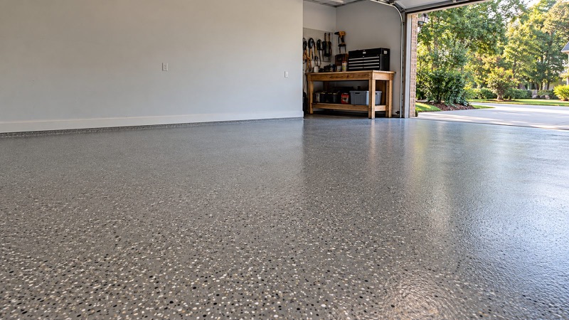 Gray flake-coated garage floor with a workbench and the garage door open to a green yard